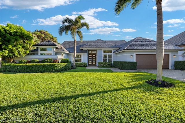 prairie-style home featuring driveway, an attached garage, french doors, a front yard, and stucco siding