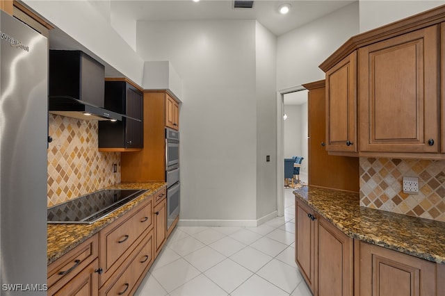 kitchen with light tile patterned floors, appliances with stainless steel finishes, brown cabinetry, and dark stone countertops