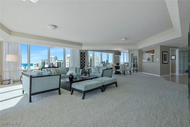 living room with a tray ceiling, a view of city, light colored carpet, and baseboards