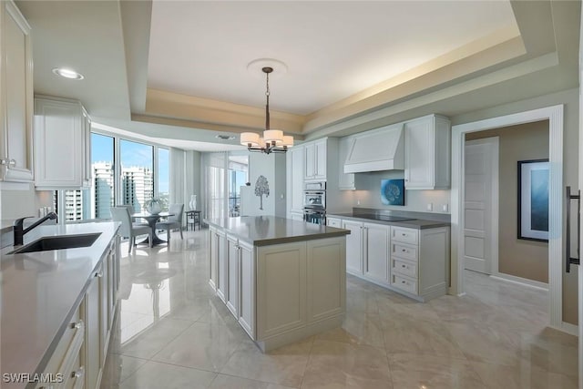 kitchen featuring a notable chandelier, a raised ceiling, custom range hood, and a sink