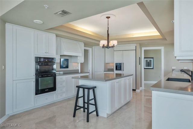 kitchen with visible vents, a tray ceiling, white cabinets, black appliances, and a sink