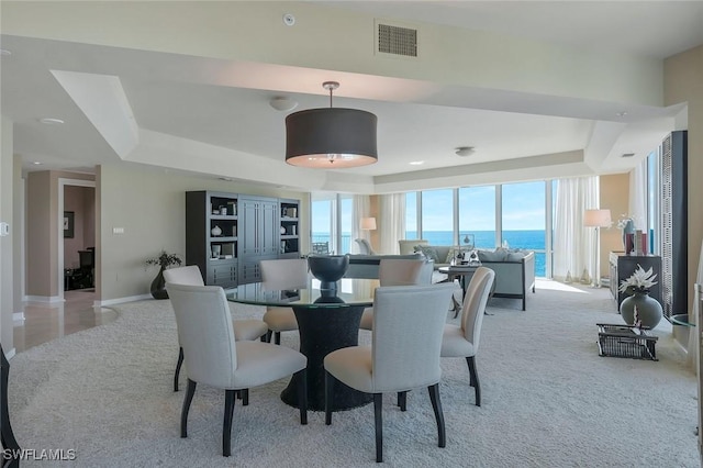 dining space with light carpet, visible vents, a raised ceiling, and baseboards