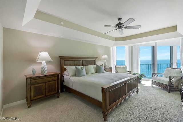 bedroom featuring light colored carpet, a tray ceiling, a ceiling fan, and a water view