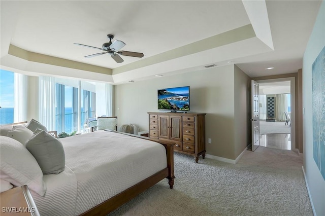 bedroom featuring a tray ceiling, light colored carpet, visible vents, and ceiling fan