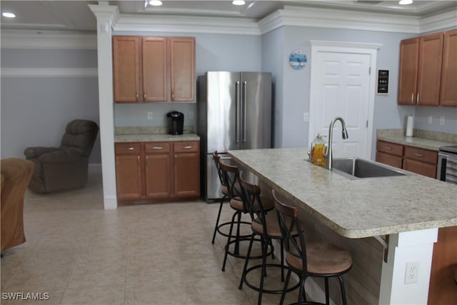 kitchen featuring a breakfast bar area, a sink, high end fridge, light countertops, and a center island with sink