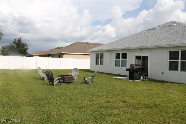 rear view of property with a yard, an outdoor fire pit, roof with shingles, and fence