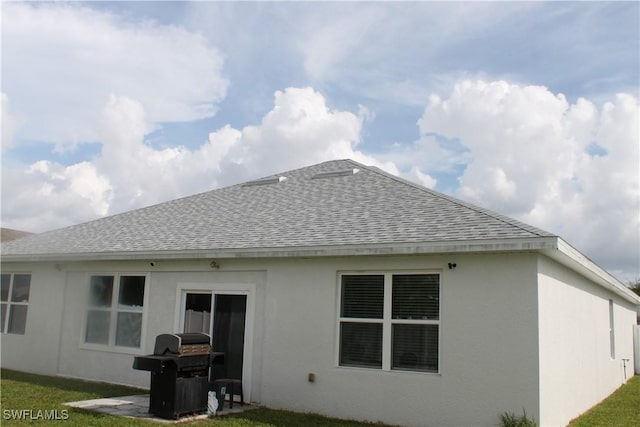 rear view of house with a yard, roof with shingles, and stucco siding