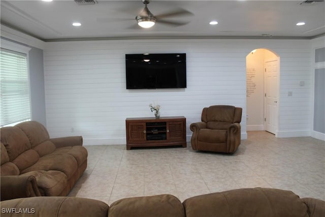 living room featuring arched walkways, light tile patterned floors, ornamental molding, a ceiling fan, and baseboards