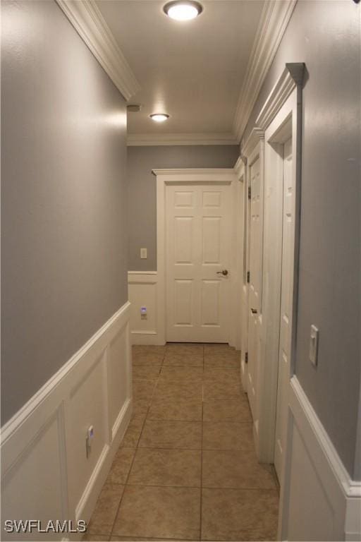 hall with wainscoting, crown molding, a decorative wall, and tile patterned floors