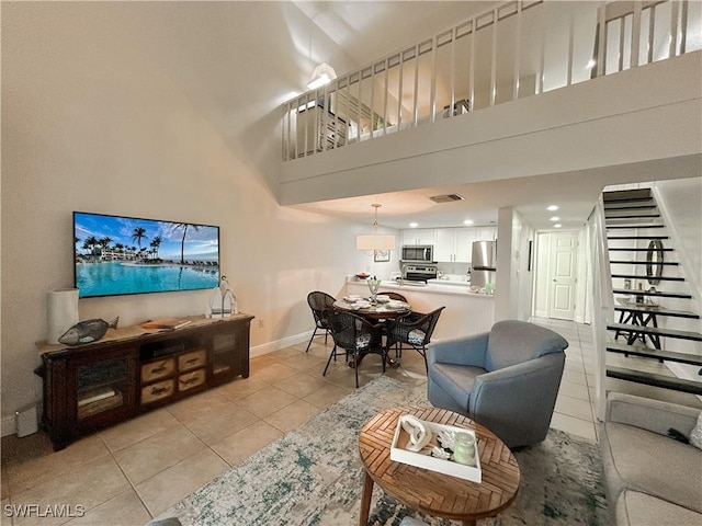 living room featuring light tile patterned floors, visible vents, stairway, a high ceiling, and baseboards