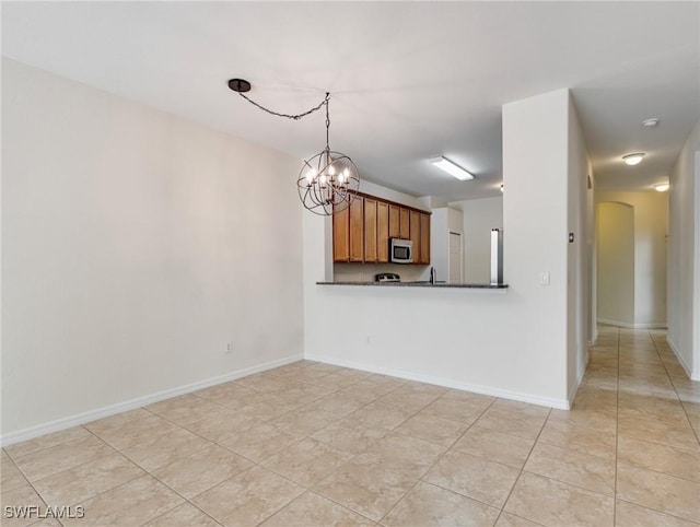 kitchen with arched walkways, a chandelier, brown cabinetry, stainless steel microwave, and dark countertops