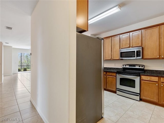 kitchen featuring light tile patterned floors, stainless steel appliances, brown cabinetry, and visible vents