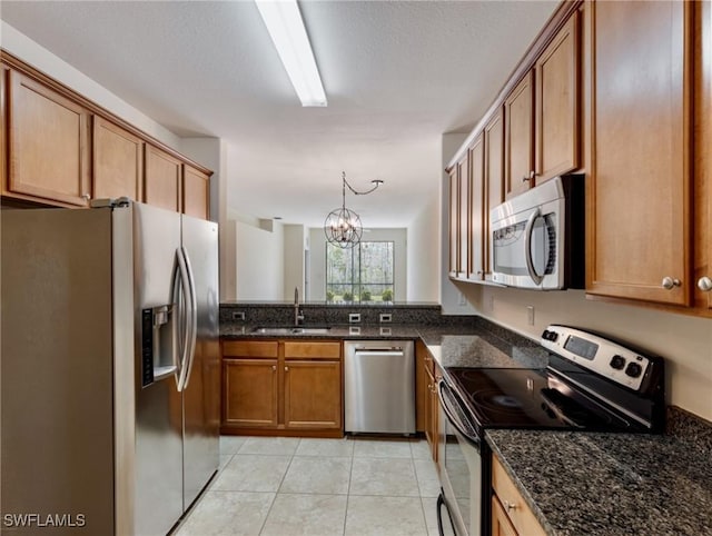 kitchen with light tile patterned flooring, a sink, appliances with stainless steel finishes, dark stone counters, and brown cabinetry