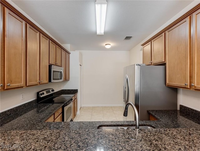 kitchen with visible vents, brown cabinetry, dark stone counters, appliances with stainless steel finishes, and a sink