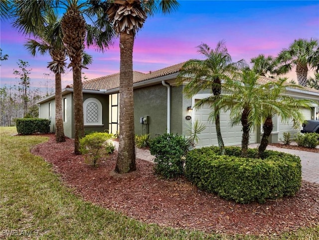 view of front of property featuring a tiled roof, decorative driveway, an attached garage, and stucco siding