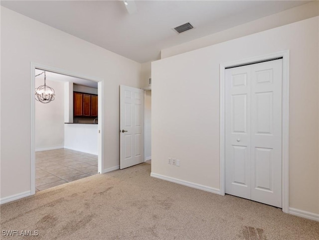 unfurnished bedroom with baseboards, visible vents, light colored carpet, an inviting chandelier, and a closet