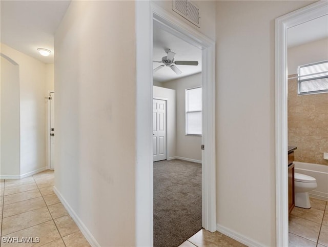 hallway with light tile patterned floors, light carpet, visible vents, and baseboards