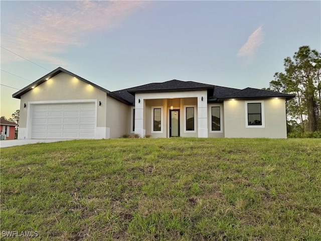 prairie-style house with a garage, a yard, driveway, and stucco siding