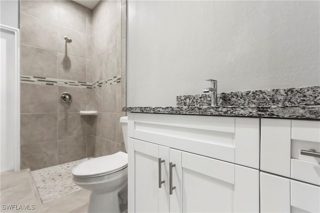 bathroom with toilet, a tile shower, and vanity