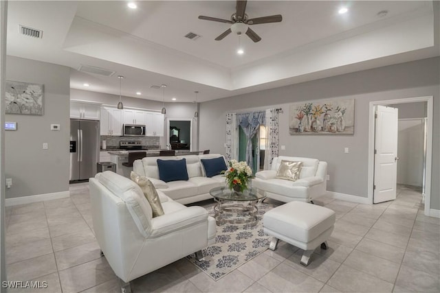 living room featuring a tray ceiling, light tile patterned flooring, and visible vents