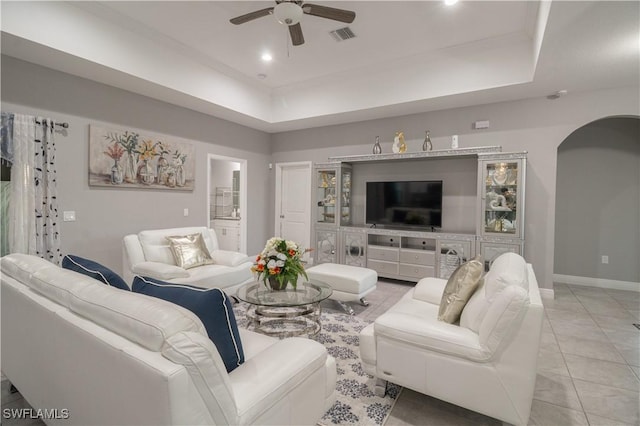 living area with a ceiling fan, arched walkways, visible vents, and a tray ceiling