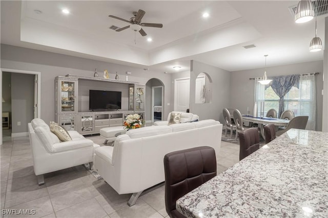 living area featuring a tray ceiling, arched walkways, recessed lighting, visible vents, and ceiling fan