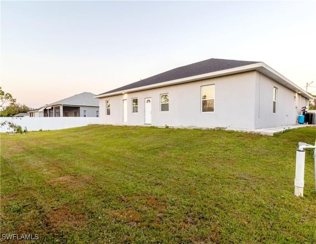 rear view of property featuring stucco siding, a yard, and fence