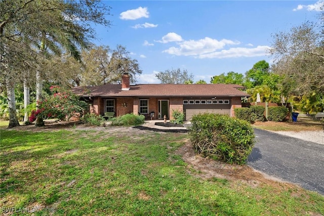 ranch-style home with brick siding, a chimney, a front yard, a garage, and driveway