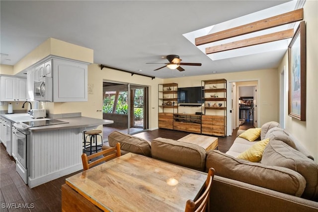 living room with a skylight, ceiling fan, and dark wood-type flooring