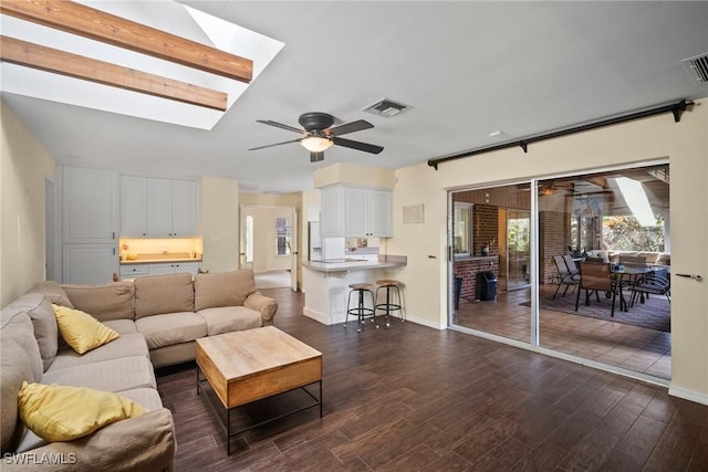 living area with a skylight, dark wood finished floors, visible vents, and a ceiling fan