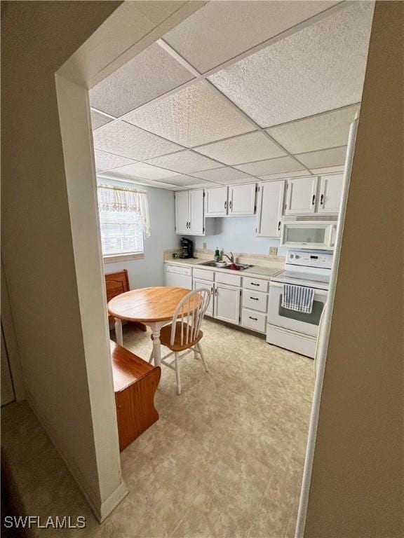 kitchen with white appliances, light countertops, a paneled ceiling, white cabinetry, and a sink