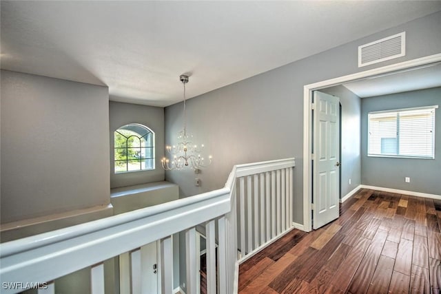 corridor featuring visible vents, an inviting chandelier, an upstairs landing, wood finished floors, and baseboards