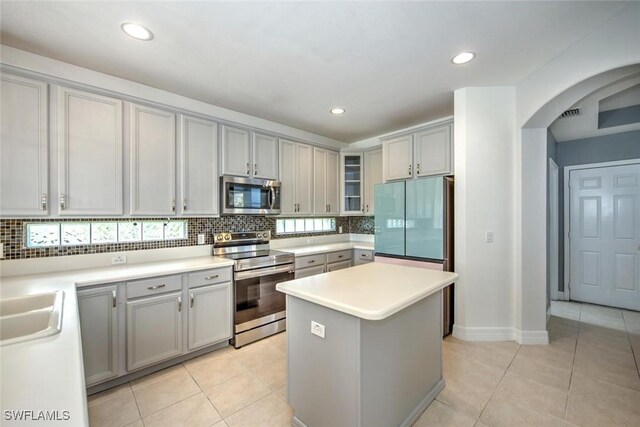 kitchen with light tile patterned floors, stainless steel appliances, backsplash, gray cabinetry, and a kitchen island