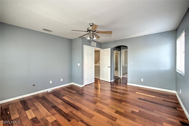 unfurnished bedroom with baseboards, visible vents, arched walkways, and wood finished floors