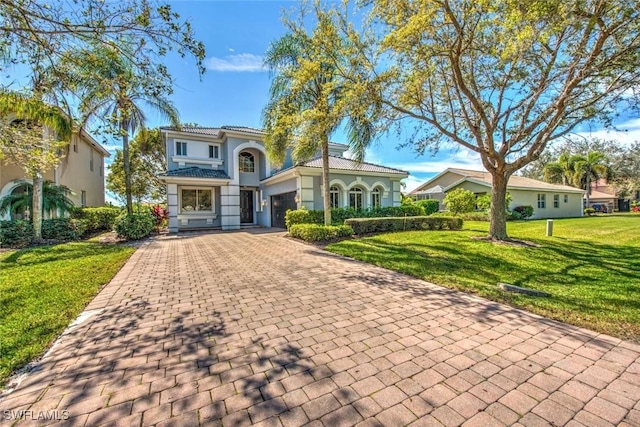 mediterranean / spanish home featuring a garage, a tile roof, decorative driveway, a front yard, and stucco siding