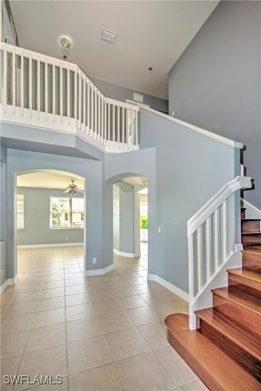 interior space with arched walkways, a high ceiling, ceiling fan, baseboards, and stairs