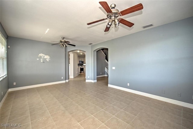 empty room featuring arched walkways, a ceiling fan, visible vents, and baseboards