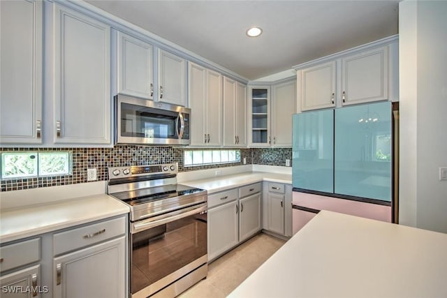 kitchen with light countertops, appliances with stainless steel finishes, gray cabinets, tasteful backsplash, and glass insert cabinets