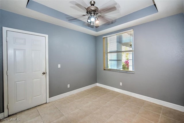 spare room featuring light tile patterned floors, a tray ceiling, a ceiling fan, and baseboards