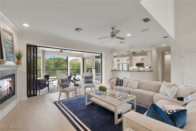 living area with a ceiling fan, visible vents, light wood-style floors, and crown molding