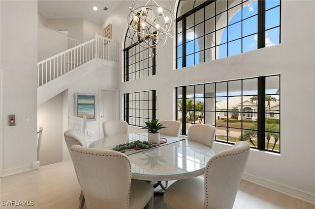 dining room featuring baseboards, wood finished floors, a towering ceiling, and a notable chandelier