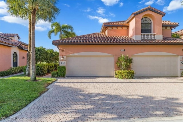 mediterranean / spanish-style home with a tiled roof, a front yard, decorative driveway, and stucco siding