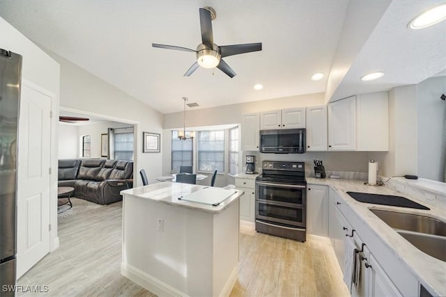 kitchen with light wood-style floors, vaulted ceiling, a kitchen island, and stainless steel appliances