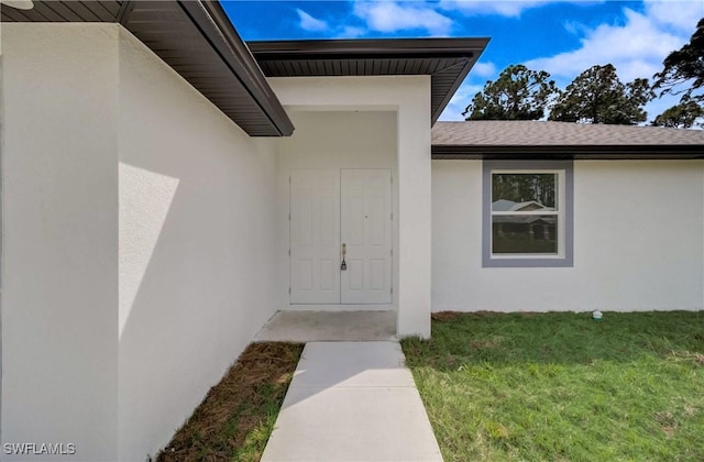 property entrance featuring a shingled roof, a yard, and stucco siding