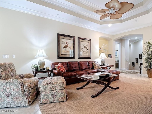 living room featuring arched walkways, light tile patterned floors, a ceiling fan, a tray ceiling, and crown molding