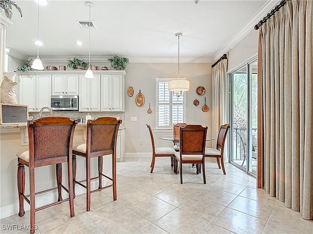 kitchen with a breakfast bar, stainless steel microwave, visible vents, ornamental molding, and baseboards