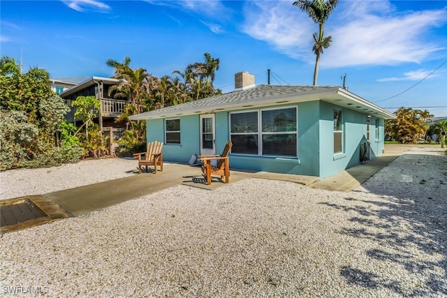 back of property featuring a patio area, roof with shingles, a chimney, and stucco siding