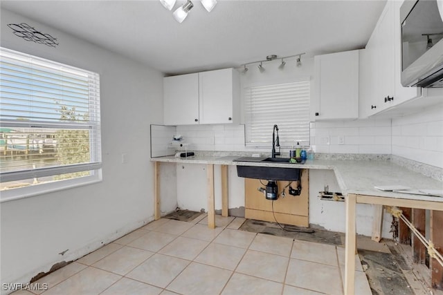 kitchen with light tile patterned floors, white cabinetry, light countertops, backsplash, and stainless steel microwave