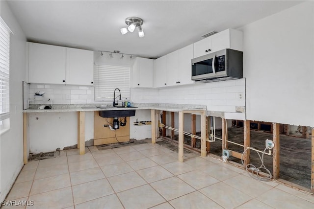 kitchen with light tile patterned floors, stainless steel microwave, backsplash, white cabinets, and a sink