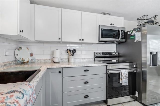 kitchen with appliances with stainless steel finishes, white cabinetry, visible vents, and light stone countertops